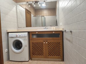 A compact bathroom with a washing machine, a sink, and a mirror.