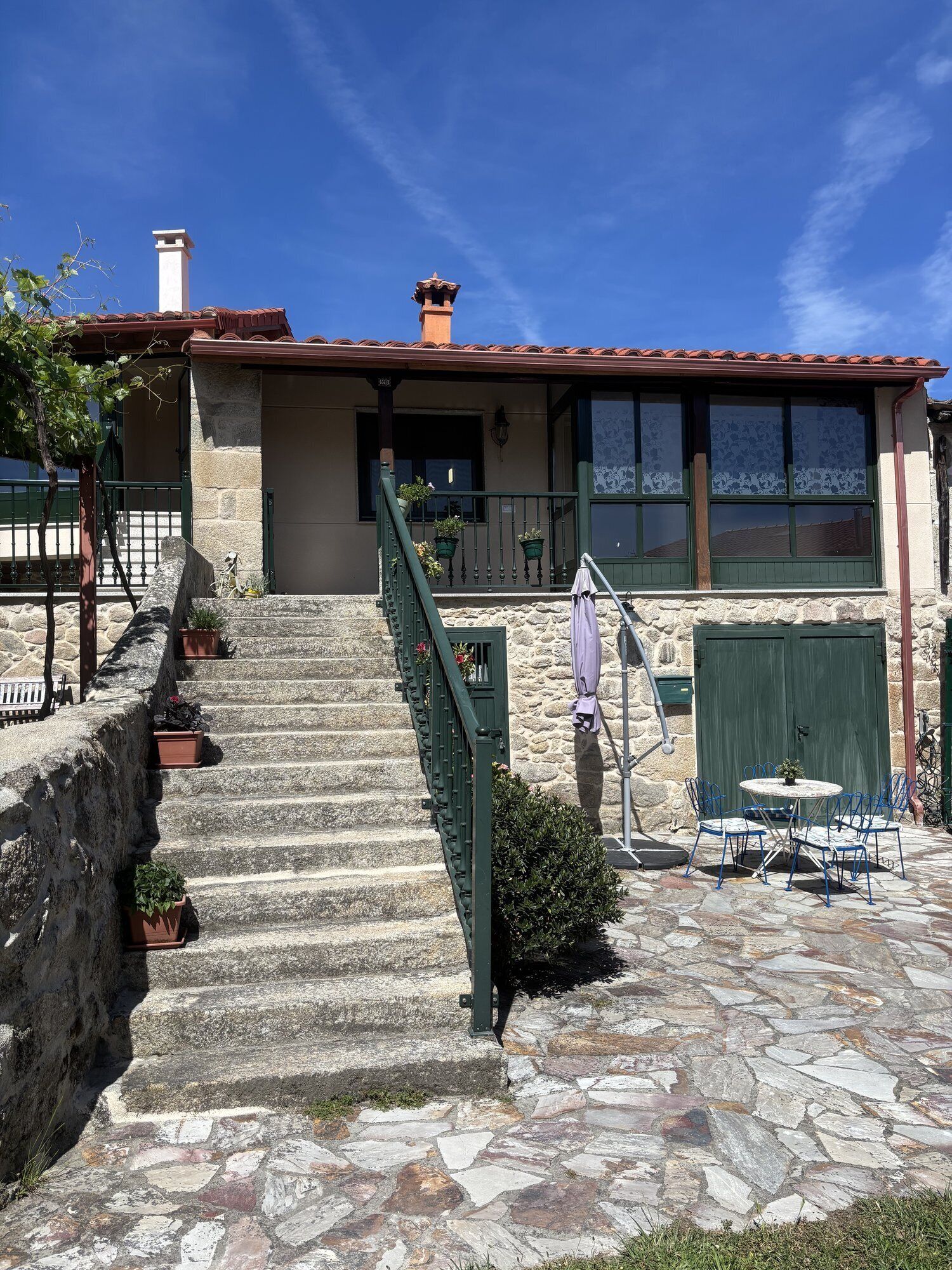 A stone staircase leading to a house with a tiled roof, a green door, and a stone wall.