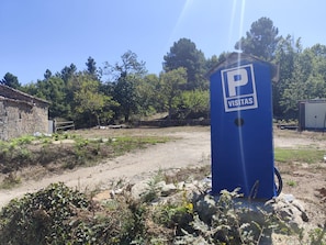 Ein blaues Parkschild mit der Aufschrift 'VISITAS', vor einer ländlichen Kulisse mit Bäumen und einem Feldweg.