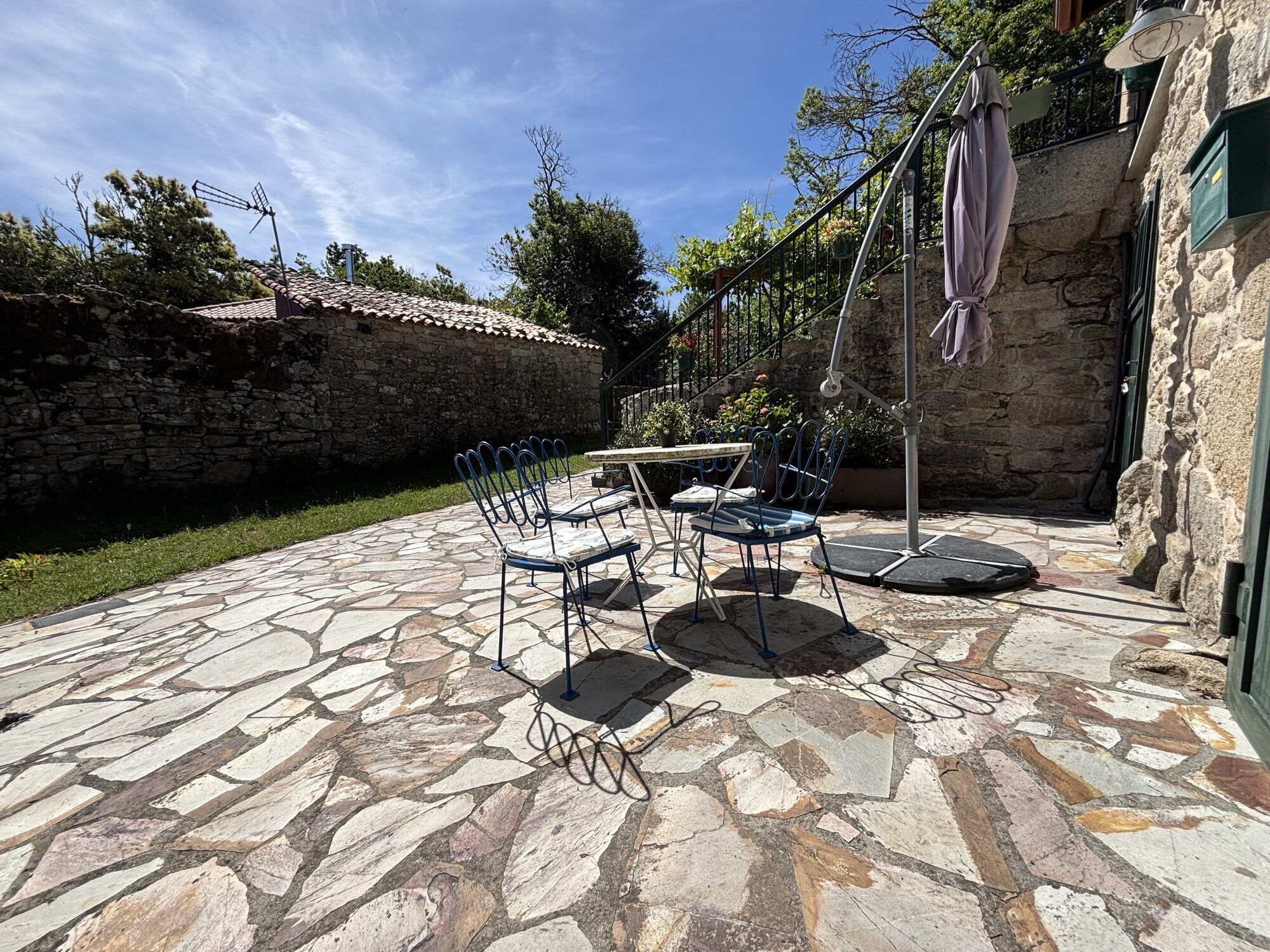 An outdoor patio with stone flooring, metal chairs, a table, and a hanging light fixture.