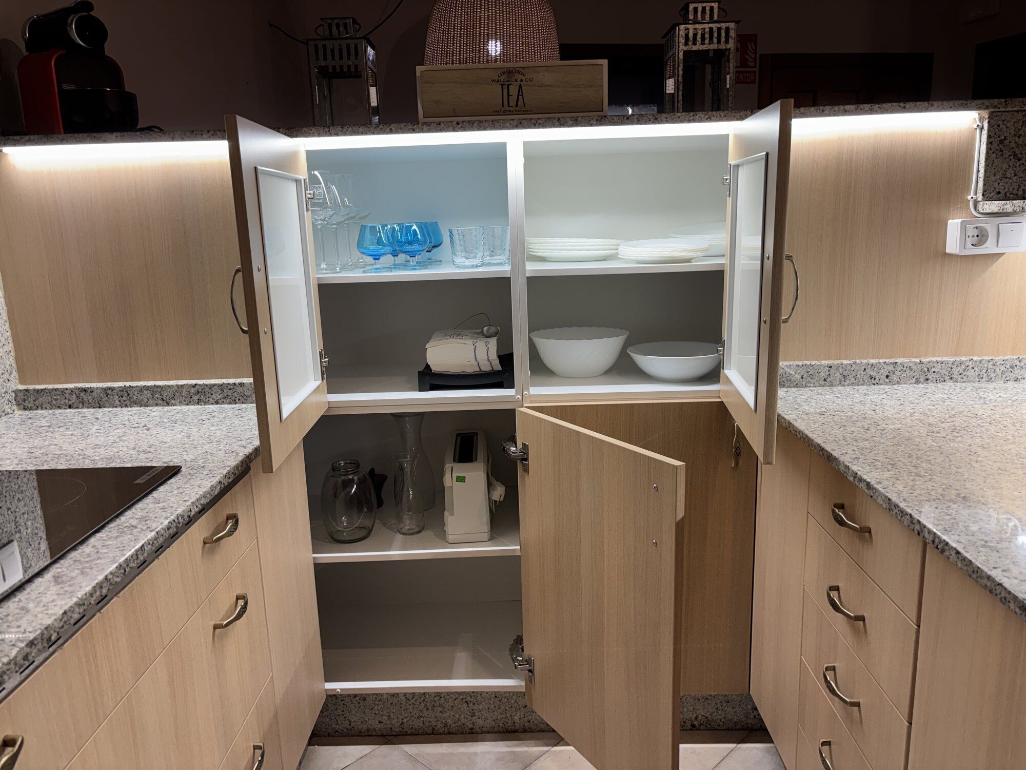 A kitchen with a built-in microwave, a coffee machine, and a tea sign on the wall.