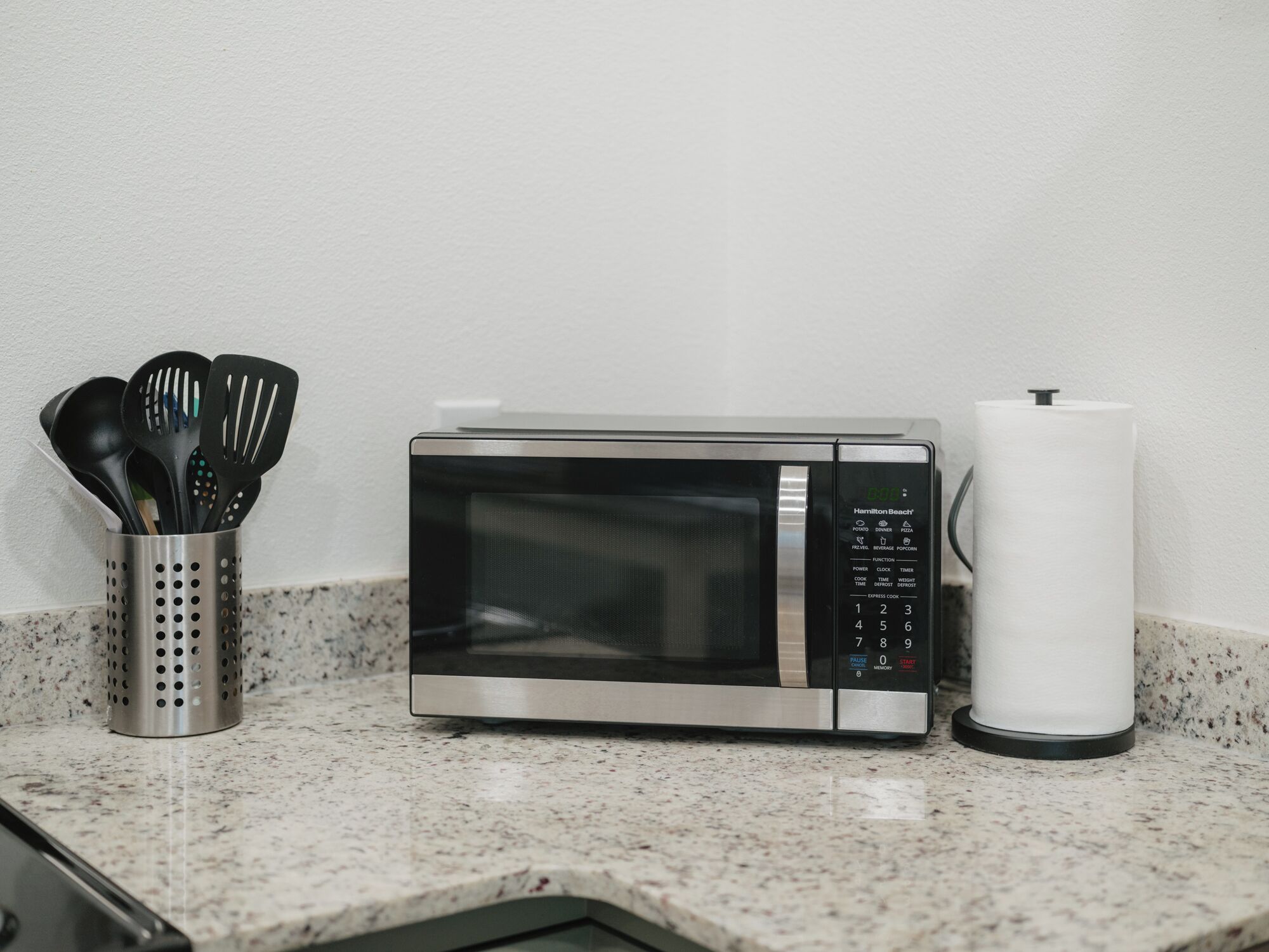 A kitchen with a microwave, a utensil holder, and a paper towel dispenser.
