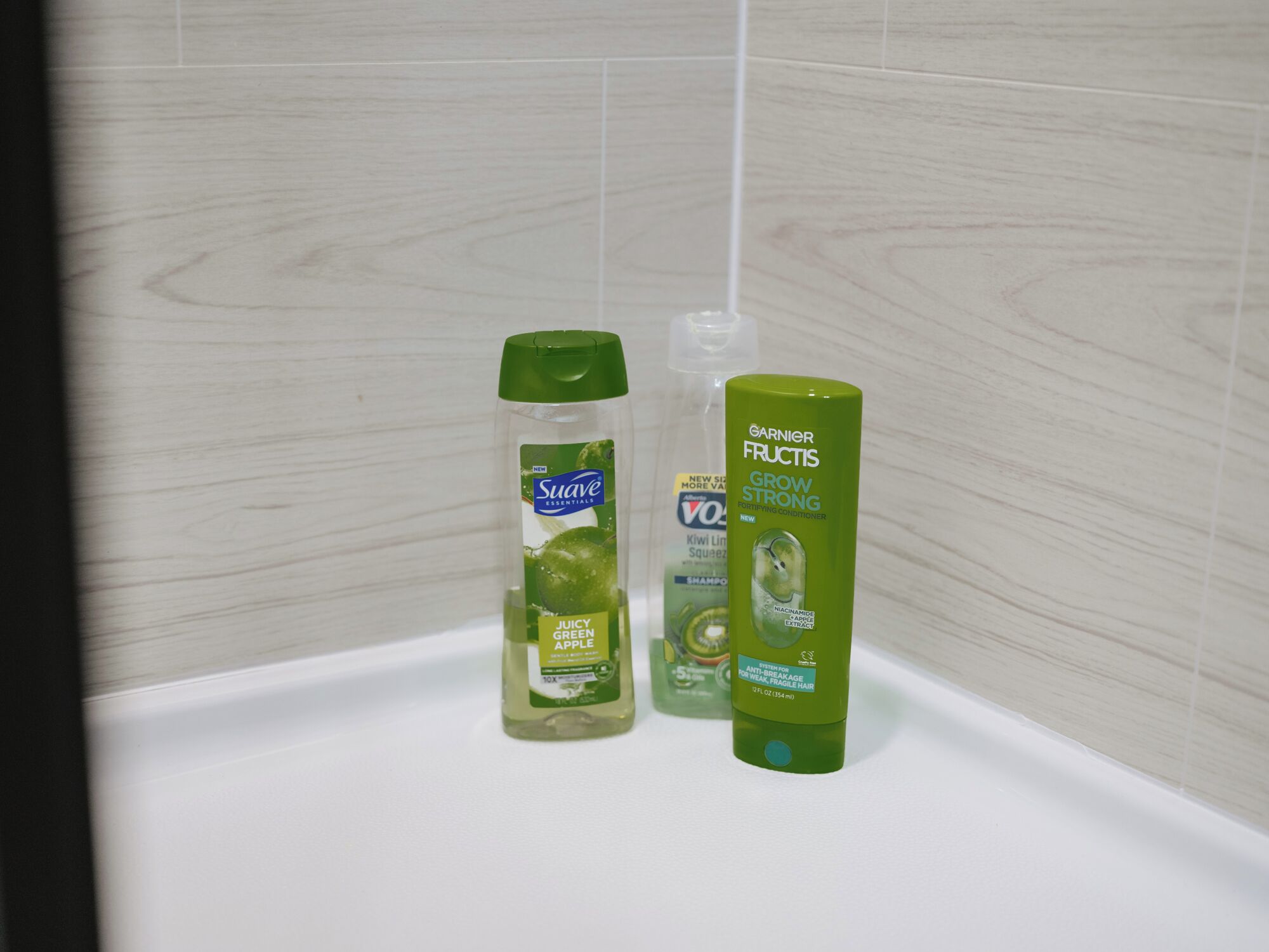 Un baño con una bañera blanca, una botella verde de champú Suave Essentials Juicy Green Apple y una botella verde de tratamiento acondicionador Garnier Fructis Grow Strong.
