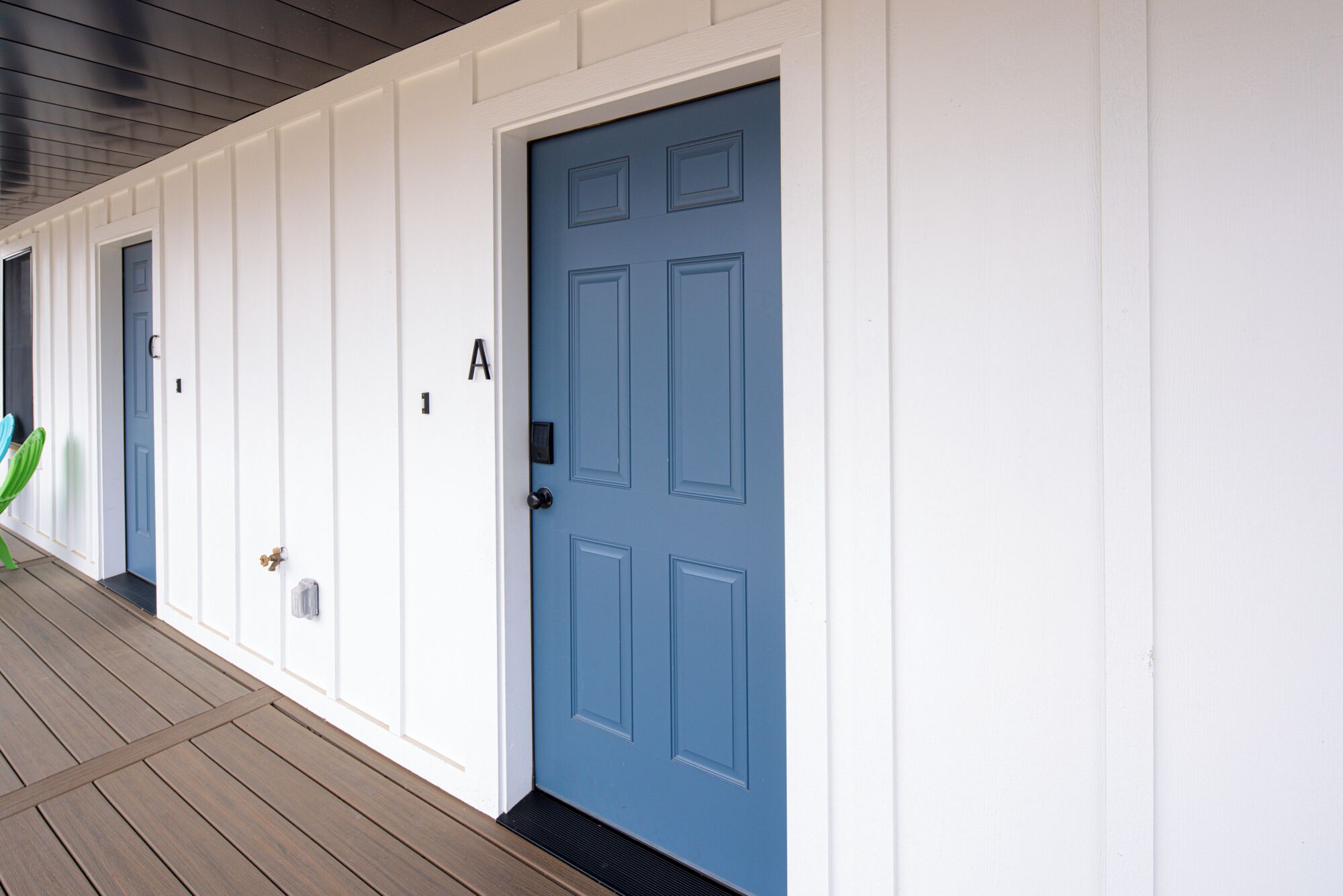 A building with a blue door labeled 'A', white exterior walls, and a wooden deck.