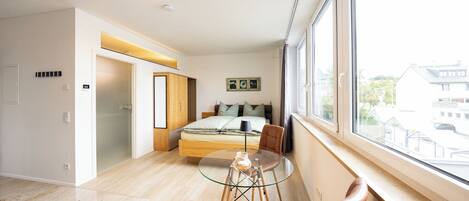 A modern bedroom with a bed, a glass table, and a view of the outside.
