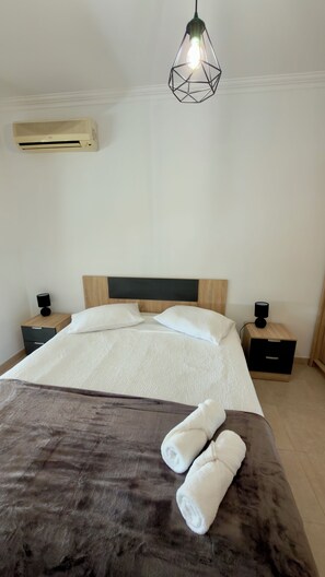 A neatly made bed with white linens, two rolled towels, a wooden headboard, bedside tables with lamps, and a hanging light fixture. - Sunny Algarve Retreat - Pool & 10 min to beach (Portimão)