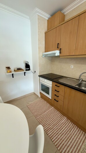 A compact kitchen with a stove, oven, and sink. There is a small shelf with jars and a coffee maker. The kitchen has wooden cabinets and a tiled backsplash. - Sunny Algarve Retreat - Pool & 10 min to beach (Portimão)