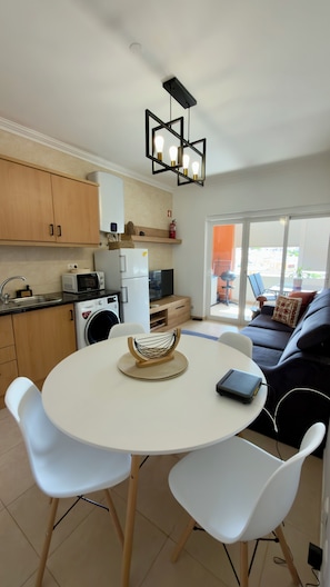 A compact living space with a kitchenette, a dining area with a round table and chairs, and a sofa in the background. - Sunny Algarve Retreat - Pool & 10 min to beach (Portimão)