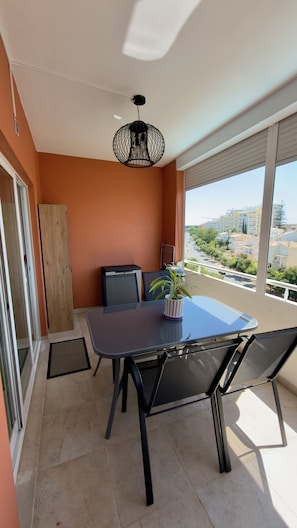 Uma varanda com mesa e cadeiras, um candeeiro pendente e vista para o horizonte urbano.