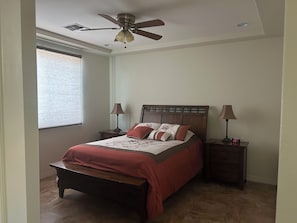 Ein Schlafzimmer mit einem Bett, zwei Nachttischen, einem Deckenventilator und einem Fenster mit Jalousien.