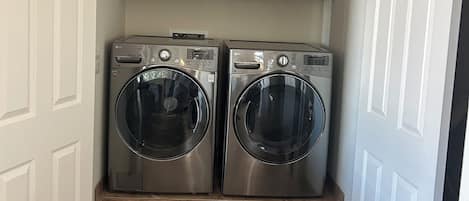 A laundry room with two front-loading washing machines, wooden cabinets above, and a tiled floor.