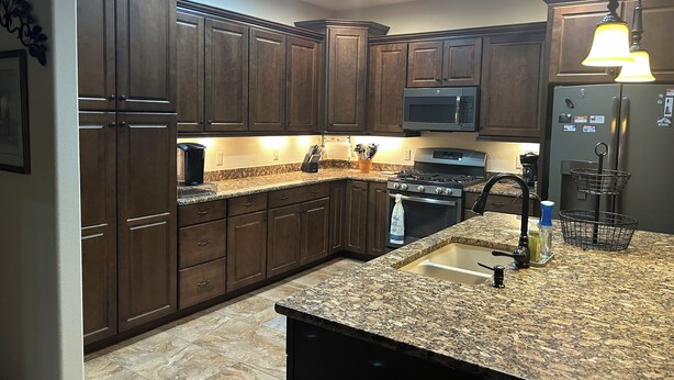 A kitchen with dark wood cabinets, granite countertops, a stainless steel refrigerator, and a gas stove. - Beautiful, furnished single level home Great for travel Nurse/corp. housing 55+ (Mesa)