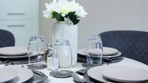 Mesa posta para refeição, com pratos, talheres e um vaso de flores.