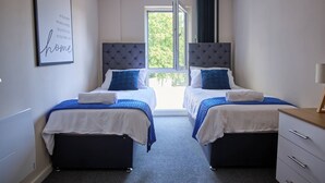 Quarto de hotel com duas camas, uma janela com vista para o verde, mesa de cabeceira e uma obra de arte na parede.