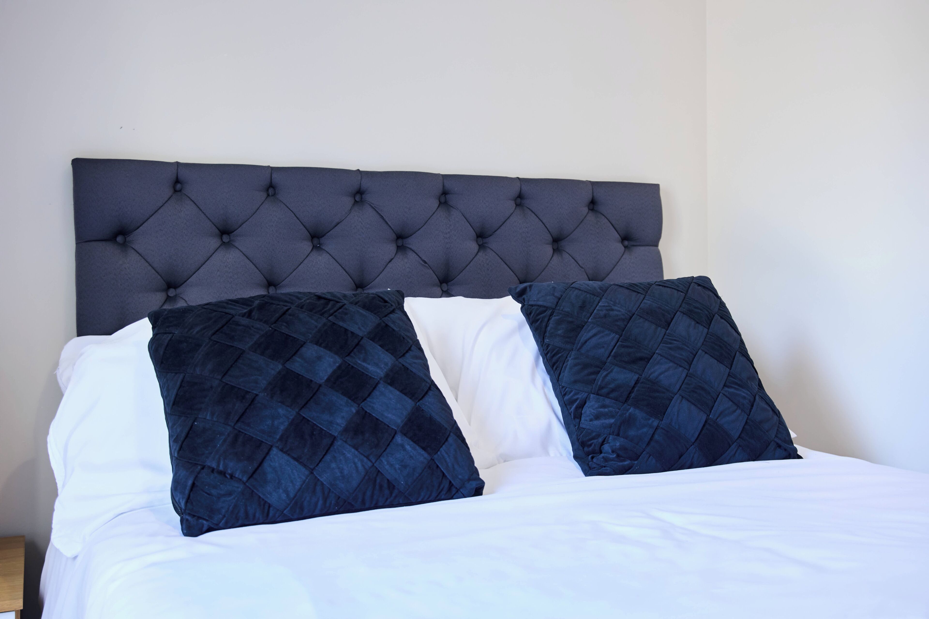 A bed with a tufted headboard, two pillows, and a wooden nightstand.
