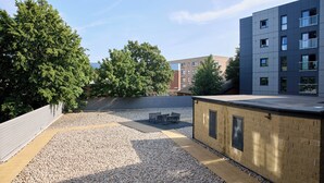 Terraço no telhado com área de cascalho, assentos e um edifício com várias janelas.