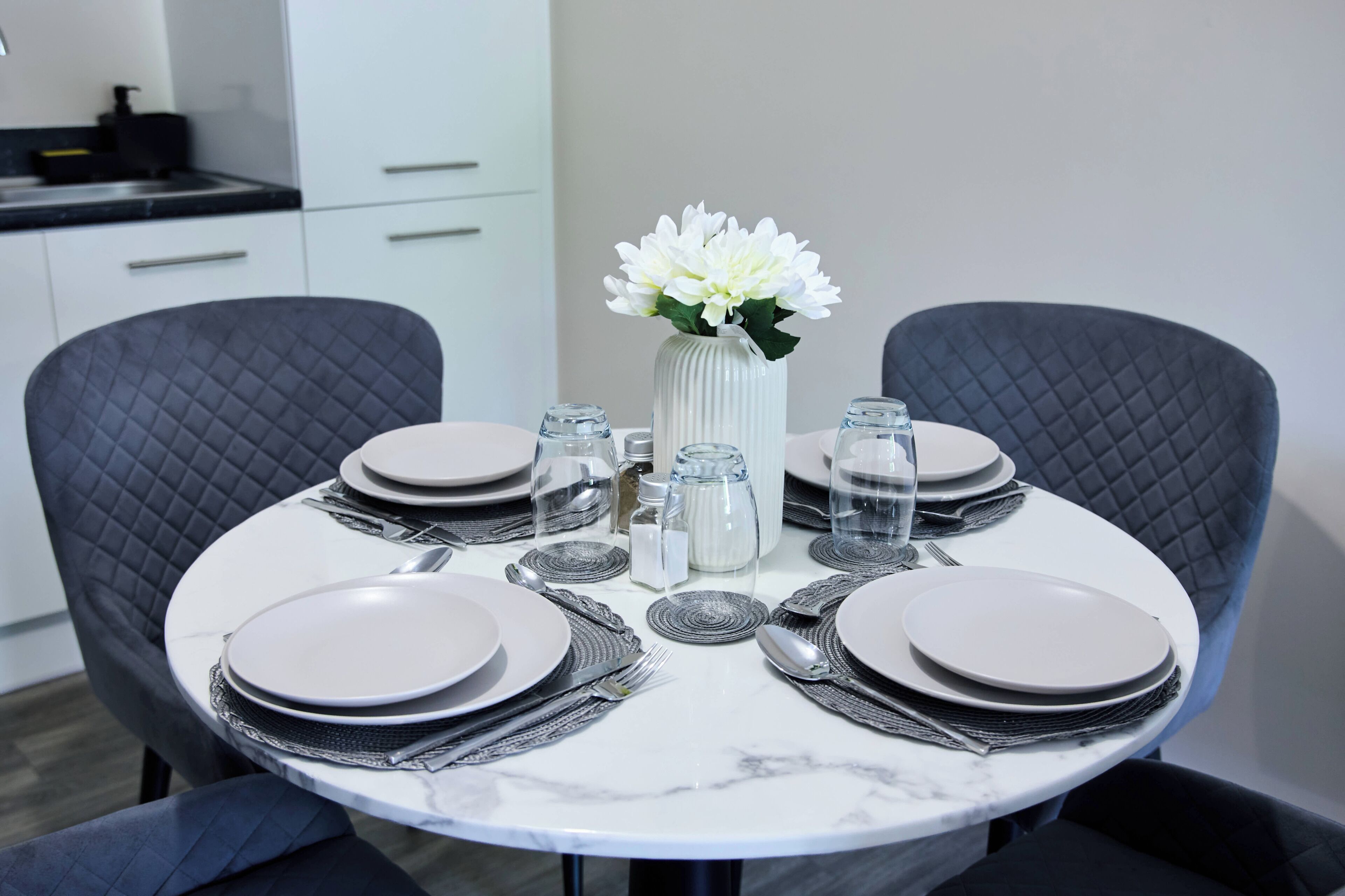 A dining table set with plates, cutlery, and a vase with flowers.