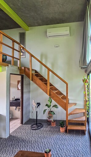 A staircase with wooden railings leading to an upper floor, a potted plant, and a fan on the floor. - Bungalow with views of the ocean and the mountains. 2 stories, studio, kitchen. Pets. (Santa Maria Tonameca.)