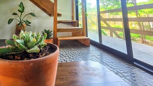 Um quarto com uma planta em vaso, um banco de madeira e vista através de uma porta de vidro.