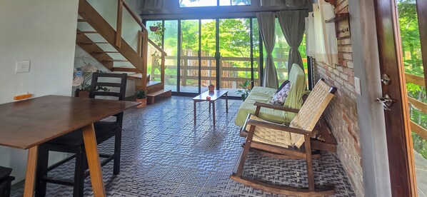 Ein Zimmer mit einer Holztreppe, einem Esstisch, einer Couch und Blick auf Grün durch große Fenster.