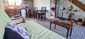 Een knus woongedeelte met een bank, een klein tafeltje, een eethoek met stoelen, een kitchenette en potplanten.