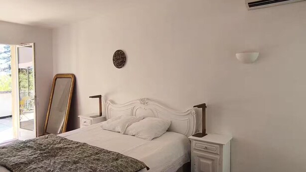 Ein Schlafzimmer mit Bett, Nachttischen, einem Spiegel, einer Wand-Klimaanlage und einer Tür zu einem Außenbereich.