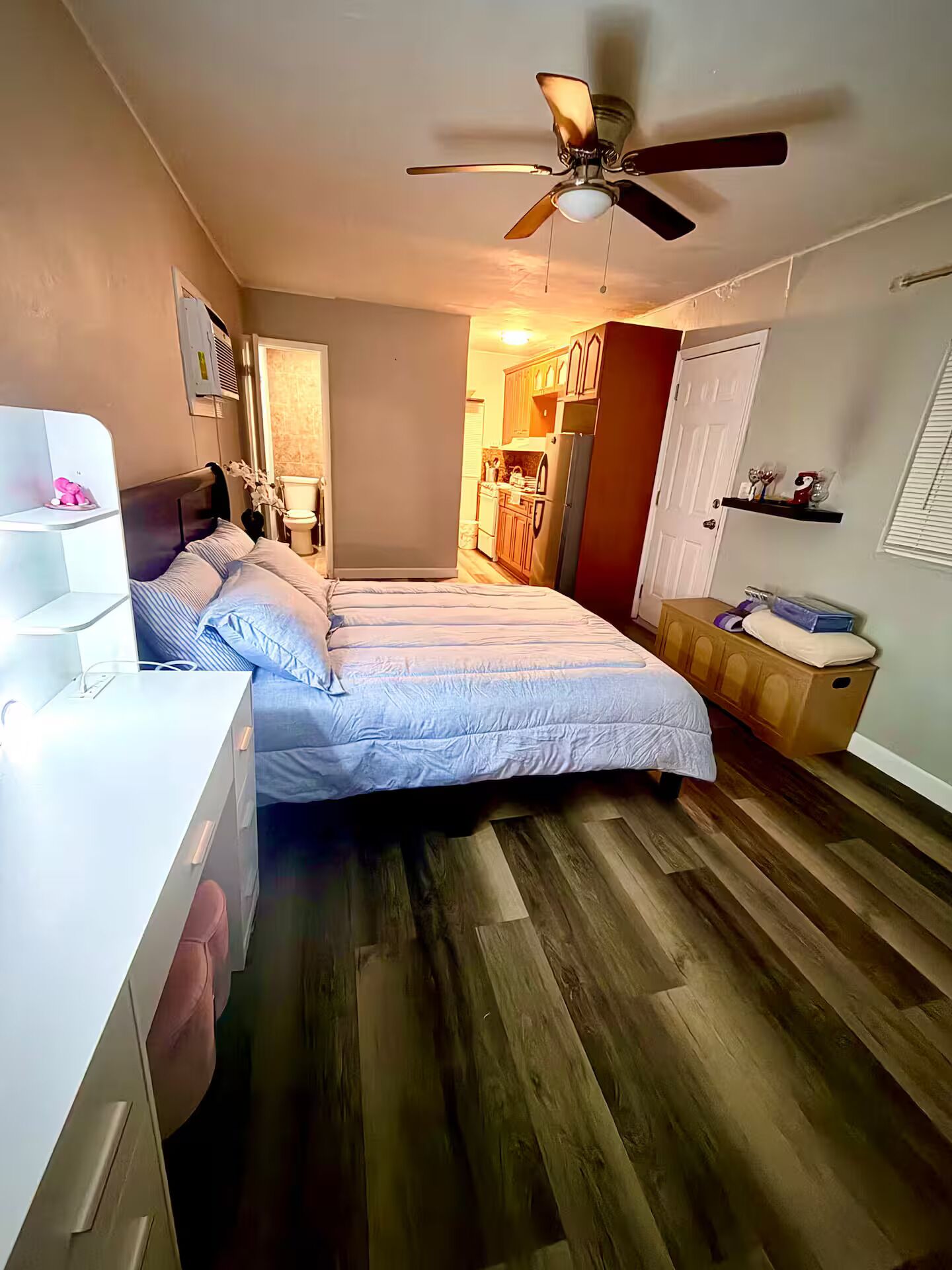 A bedroom with a bed, a desk, a ceiling fan, and a bathroom visible through an open door.