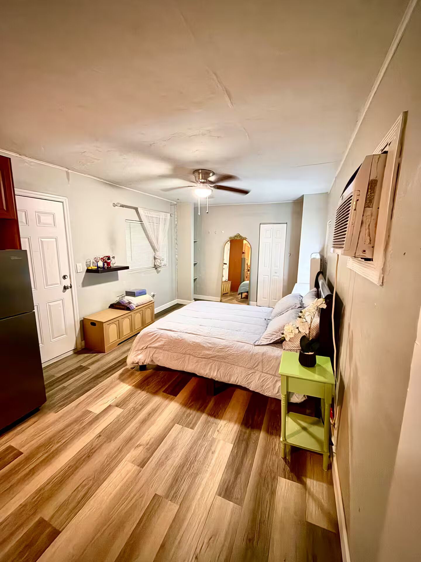 A bedroom with a bed, a ceiling fan, a nightstand, and a refrigerator.