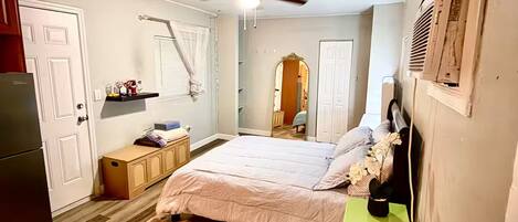 A bedroom with a bed, a ceiling fan, a nightstand, and a refrigerator.