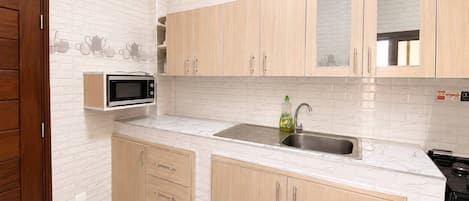A kitchen with white marble countertops, wooden cabinets, a built-in microwave, and a stainless steel sink.
