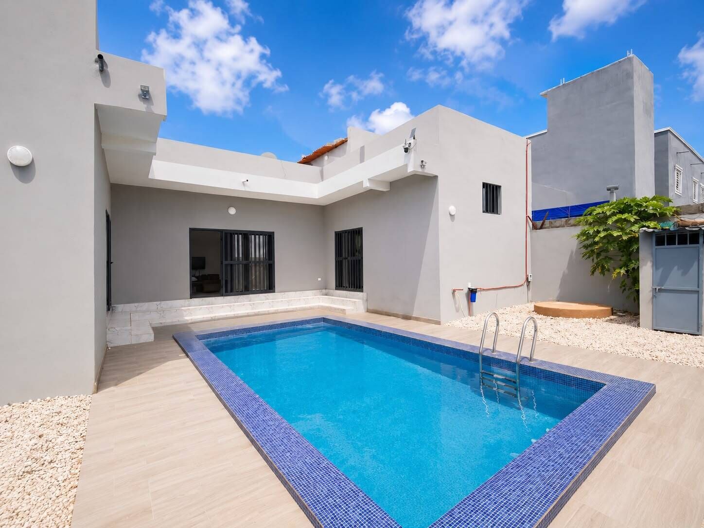 Ein moderner Außenpool mit klarem, blauem Wasser, umgeben von einer hellen Poolterrasse und einem Gebäude mit flachem Dach.