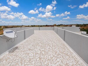 Terraza en la azotea con antena parabólica, suelo de baldosas blancas y cielo despejado.