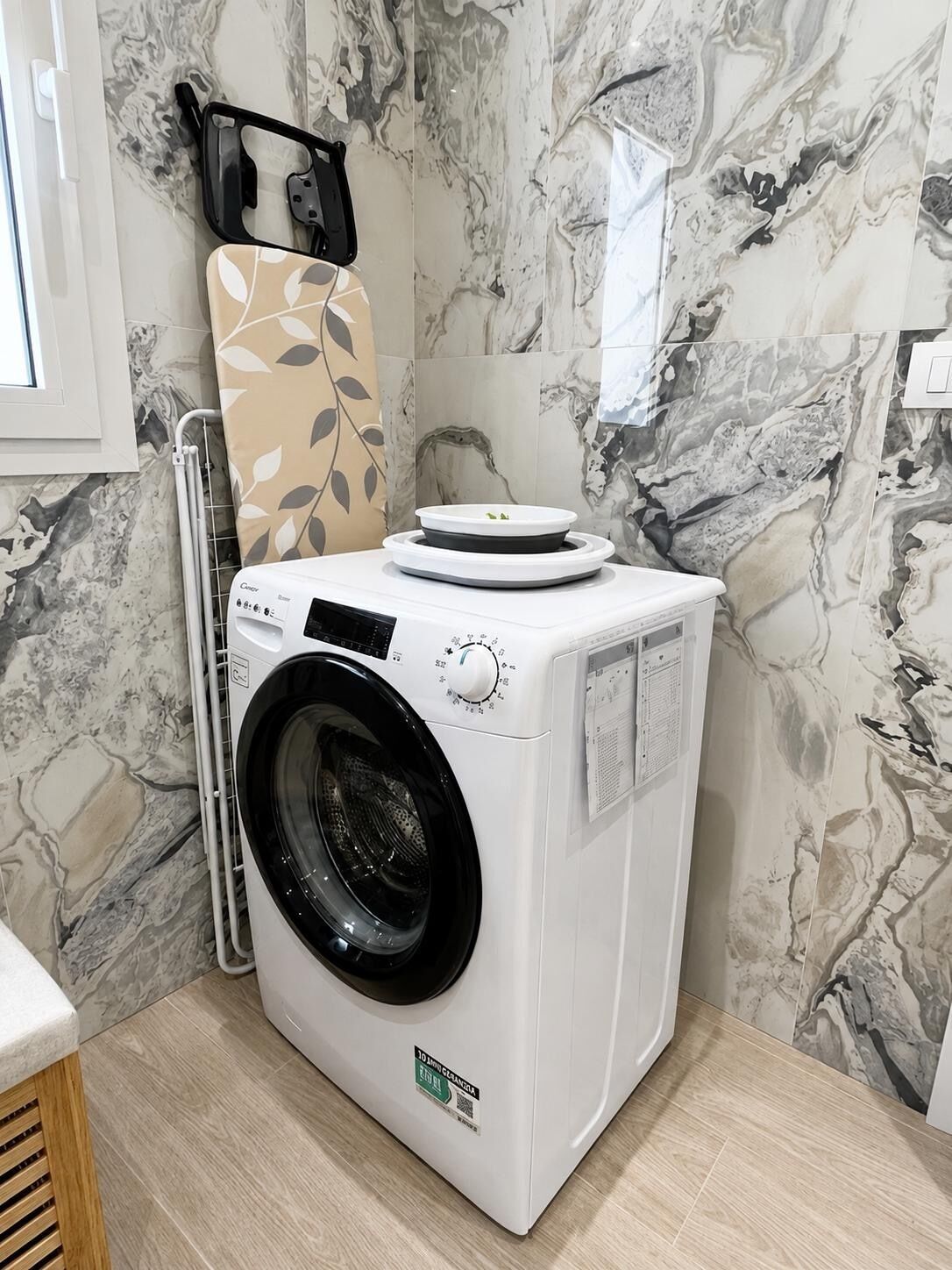 A front-loading washing machine in a bathroom with marble-patterned walls.
