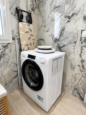 A front-loading washing machine in a bathroom with marble-patterned walls. - Relaxation, comfort, and nature, with on-site parking and a terrace, just 5 minutes from the beach. (Trappitello)