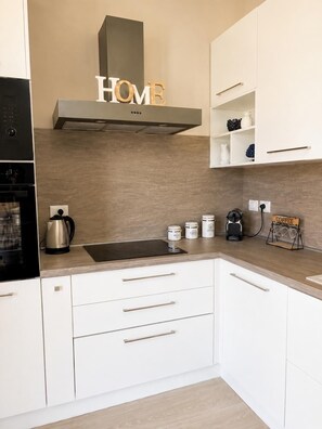 Eine moderne Küche mit weißen Schränken, einer Edelstahl-Dunstabzugshaube, einer Kaffeestation und einem Schild mit der Aufschrift 'HOME' über der Haube.