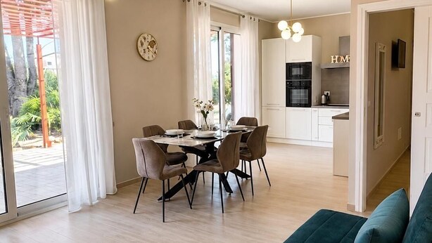 Ett modernt vardagsrum med matplats, kök och en sittgrupp med soffa och ett sidobord.