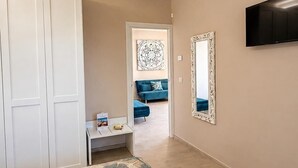 Ett sovrum med en säng, en garderob, ett skrivbord, en spegel, en tv och en hall som leder till ett vardagsrum.