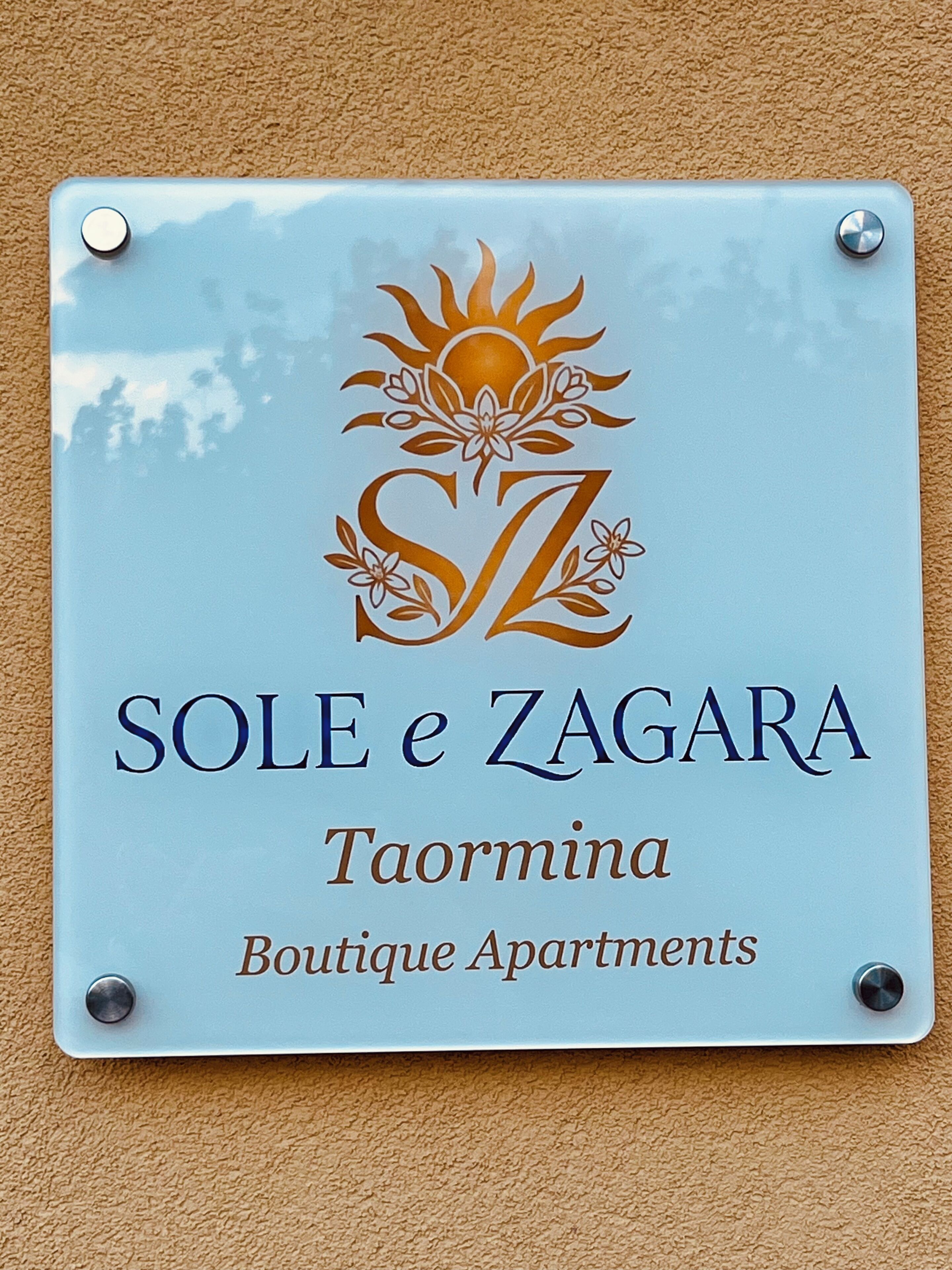Una señal para 'SOLE e ZAGARA Taormina Boutique Apartments' con un diseño de sol y motivos florales.