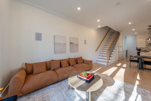 A modern living room with a sofa, a coffee table with a book, and a staircase leading to another room. - Spacious 5-bedroom townhome in Amazing Jersey City with Rooftop (Jersey City)