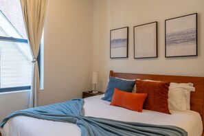 A hotel room with a bed, pillows, a bedside table with a lamp, and three framed artworks on the wall. - Spacious 5-bedroom townhome in Amazing Jersey City with Rooftop (Jersey City)