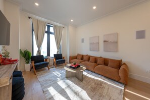 A modern living room with a sofa, two armchairs, a coffee table, and a TV mounted on the wall. - Spacious 5-bedroom townhome in Amazing Jersey City with Rooftop (Jersey City)