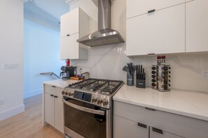 Une cuisine moderne équipée d’une cuisinière à gaz, d’un four, d’une hotte en acier inoxydable et d’une machine à café.
