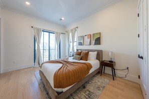 A bedroom with a large bed, a bedside table, a nightstand, a window with curtains, and a wall-mounted artwork. - Spacious 5-bedroom townhome in Amazing Jersey City with Rooftop (Jersey City)