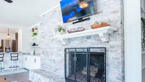 A living room with a fireplace, a mounted television, and a dining area with chairs and a table.