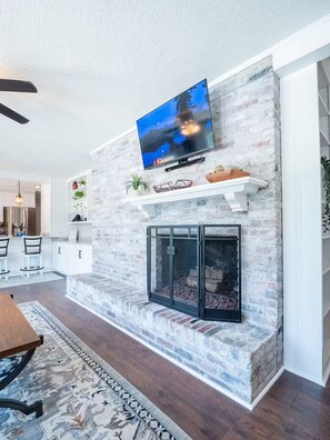 A living room with a fireplace, a mounted television, and a dining area with chairs and a table.