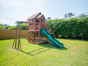 A wooden playhouse with a slide and a ladder.