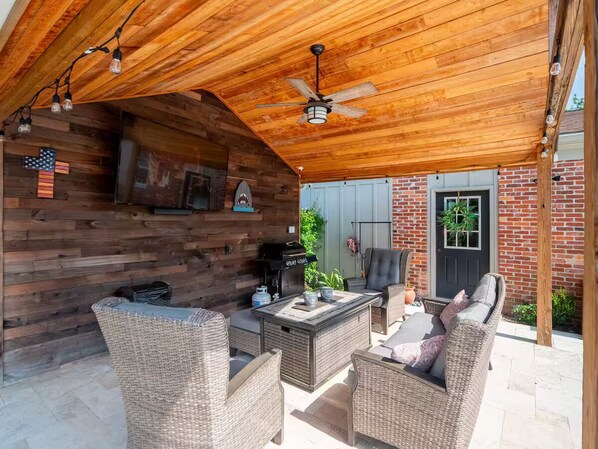 An outdoor patio with wicker furniture, a grill, and a ceiling fan.