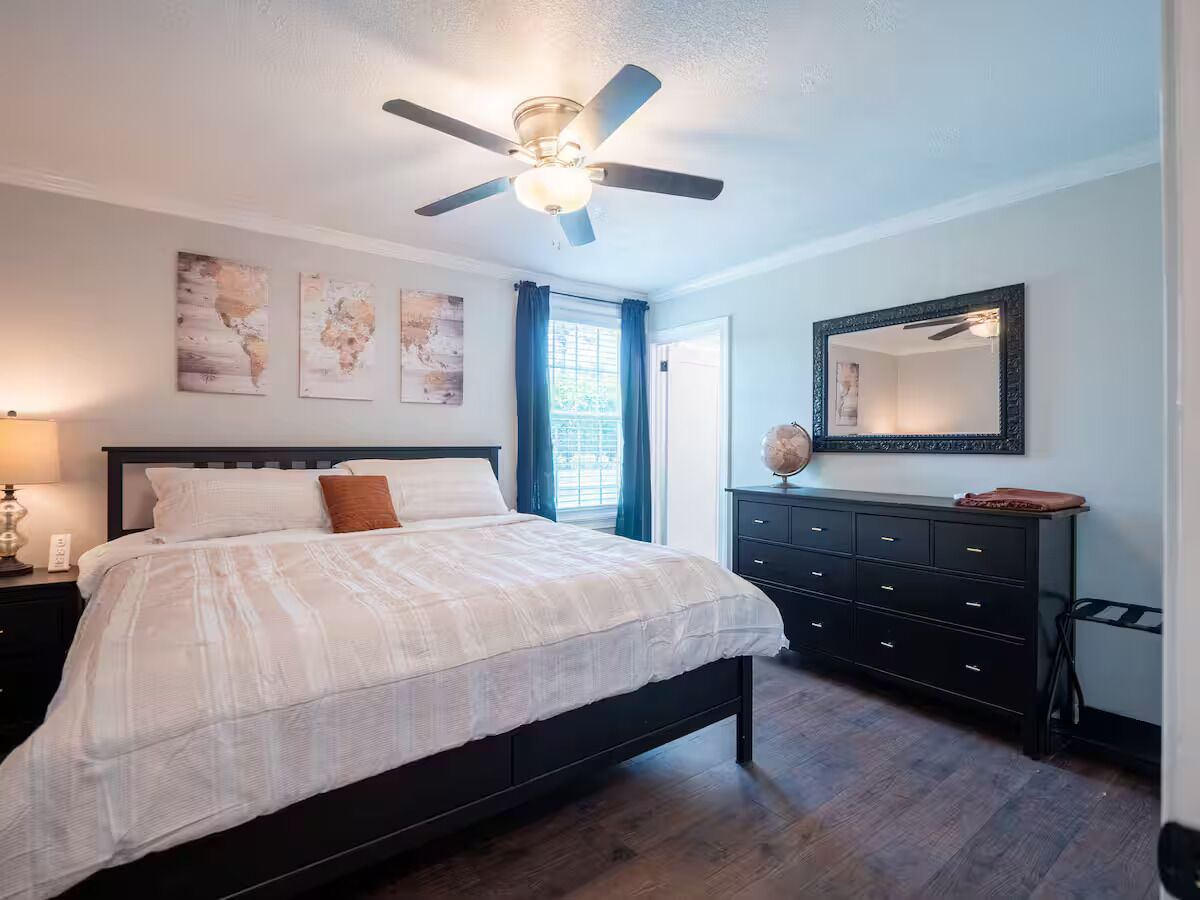 A bedroom with a bed, a dresser, a ceiling fan, and artwork on the wall.