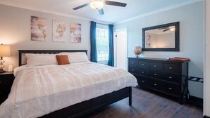 A bedroom with a bed, a dresser, a ceiling fan, and artwork on the wall.