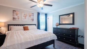 A bedroom with a bed, a dresser, a ceiling fan, and artwork on the wall.